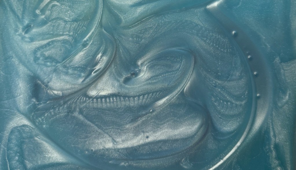 Teal-green silicone back layer marbled with pearlescent swirls in an acrylic blank; faint gold veining and dispersed dark-blue ‘antimatter’ glitter