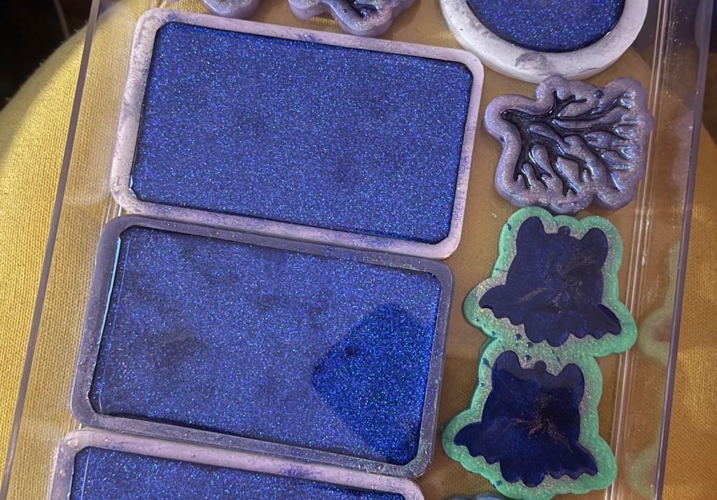 A collection of blue glittery resin molds arranged in a clear container, featuring rectangular shapes and various decorative designs.