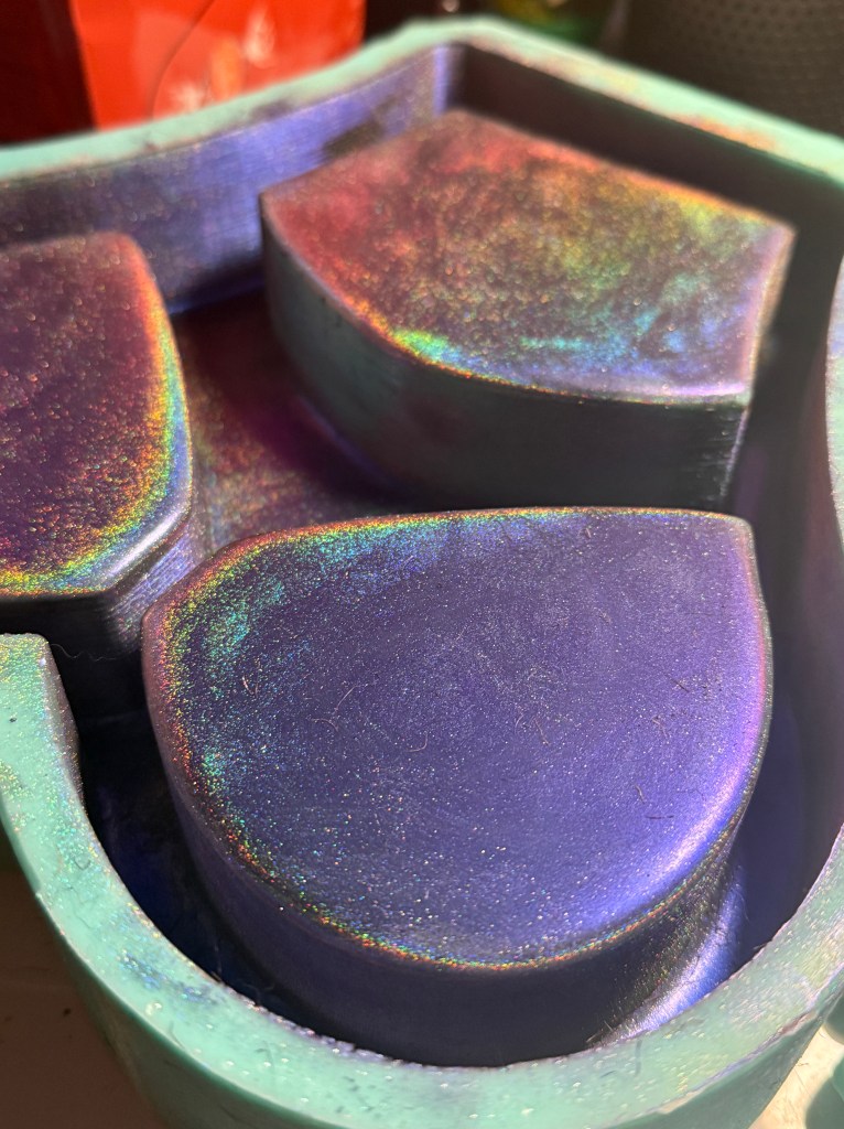 Close-up view of a colorful, iridescent mold with three distinct sections, featuring shimmering purple and turquoise hues.