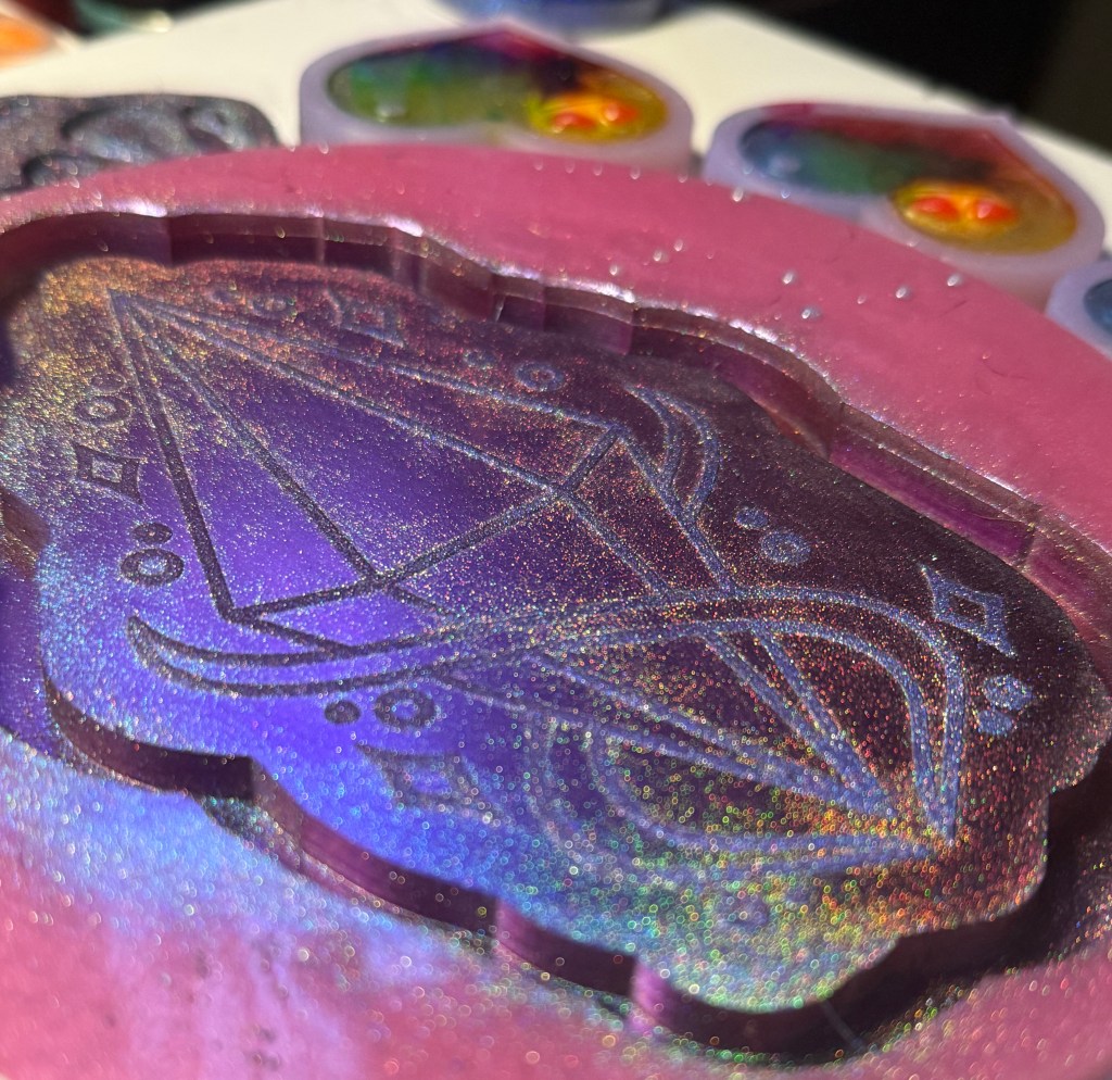 Close-up of a resin mold featuring a holographic design with geometric patterns and swirls, set against a pink outline.